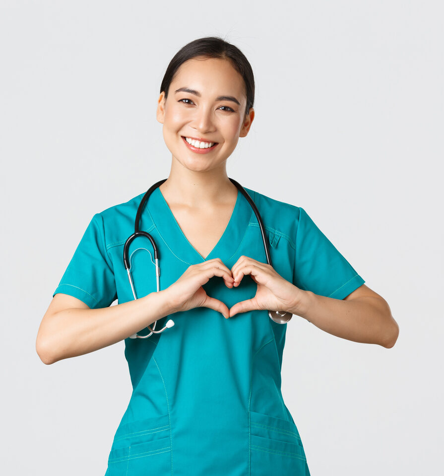 Covid-19, healthcare workers, pandemic concept. Lovely caring asian doctor, female nurse in scrubs showing heart gesture and smiling, taking care of patients with love, white background